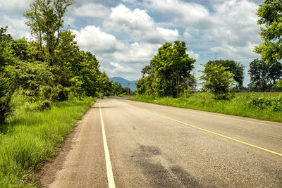 Empty road along trees and plants against sky