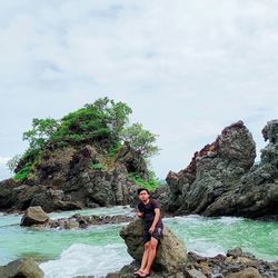 Portrait of young woman on rock against sky