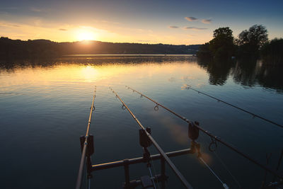 Fishing rods over lake against sky during sunset