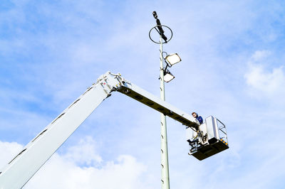 Low angle view of man standing in cherry picker against sky