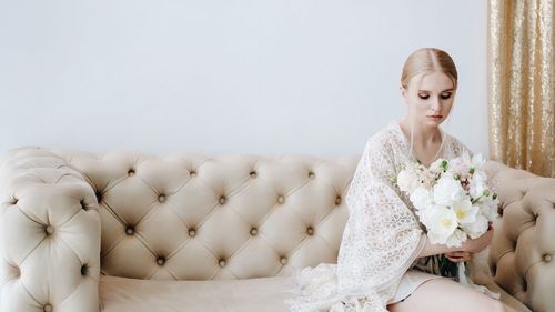 Young woman holding flowers while sitting on sofa