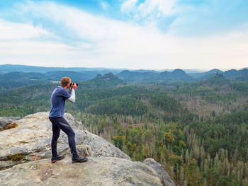 Man takes photo of landscape. photographer with eye at viewfinder of camera on stay on cliff