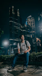 Young man sitting on seat in city at night