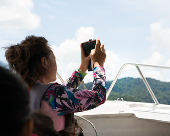 Woman photographing while using smart phone against sky