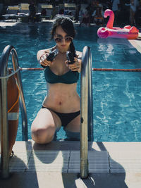 Portrait of woman aiming guns while standing in swimming pool