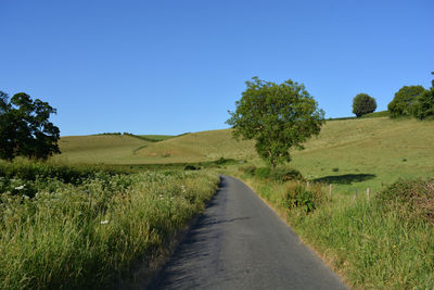 Dirt road amidst field against clear blue sky