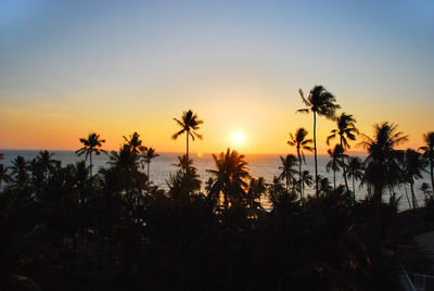 Silhouette palm trees by sea against romantic sky at sunset