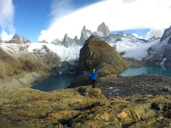 Man standing on rock by lake against sky