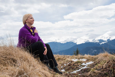 Portrait of young man sitting on mountain against sky