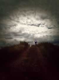 People walking on grassy field against cloudy sky