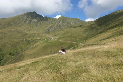 Side view of man sitting on mountains against sky