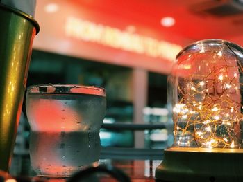 Close-up of drink glass and illuminated string light on table