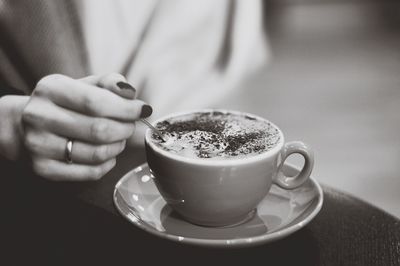 Cropped image of woman holding spoon in coffee at cafe
