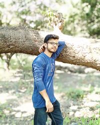 Portrait of young man standing on tree trunk