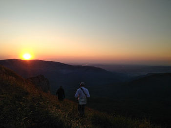 Rear view of man standing on mountain against sky during sunset