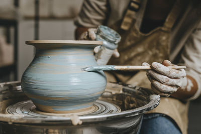 Hand's of potter painting pot on pottery wheel at workshop