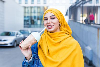 Portrait of young woman standing against building