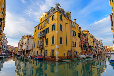 Boats moored on canal by buildings against sky in city