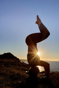 Inverted yoga pose of a woman at sunrise outside with a sun star.