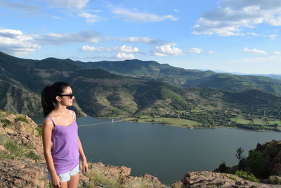 Young woman standing on mountain against sky and lake