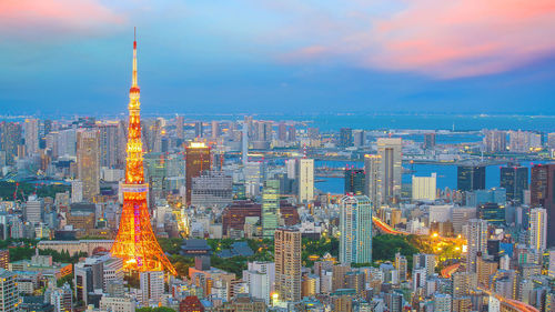 Illuminated buildings in city against cloudy sky