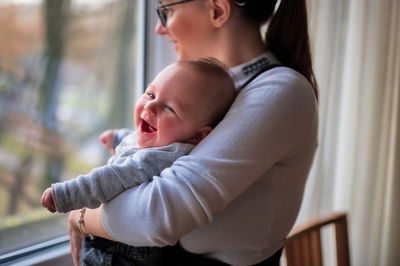 Mother standing by the window and holding cute little baby