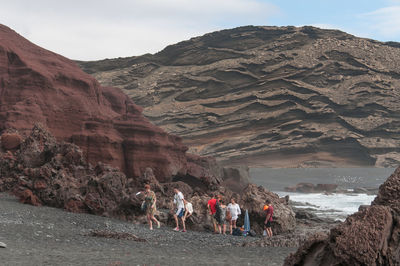 People on rocks by mountains against sky