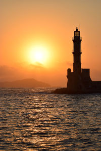 Lighthouse by sea against sky during sunset