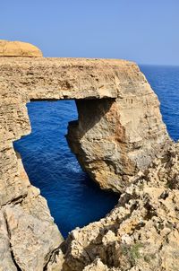 Rock formation by sea against clear blue sky