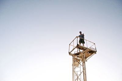 Low angle view of male hiker standing on observation point against clear sky