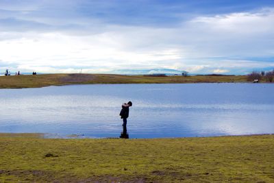 Boy standing amidst lake at park against cloudy sky