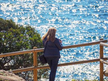 Rear view of woman standing by railing against sea