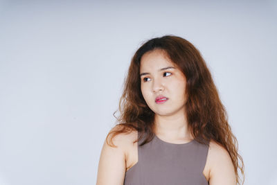 Young woman making face while standing against gray background
