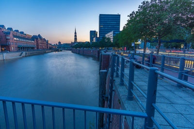 Bridge over river by buildings against sky at dusk