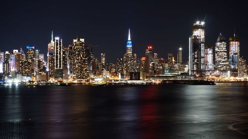 Illuminated buildings by river against sky at night
