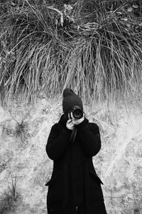 Woman photographing with camera while standing on field