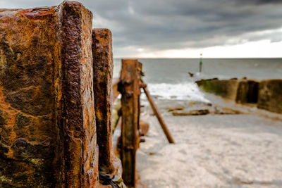 Close-up of rusty wooden post at beach against sky