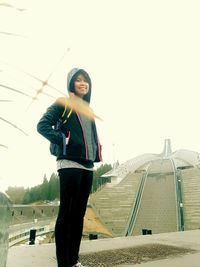 Portrait of young woman standing against sky in city