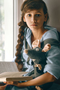 Portrait of girl with stuffed toy holding book at home