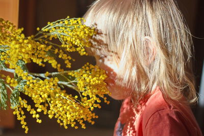 Close-up side view of baby girl smelling yellow flowering plants at home