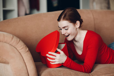 Young woman holding heart shape while sitting on sofa at home