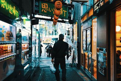 Rear view of man walking on street amidst buildings in city