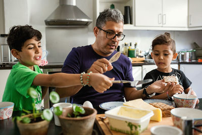 Father and sons applying butter on crackers at dining table