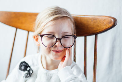 Close-up of cute girl wearing big eyeglasses while sitting on chair at home