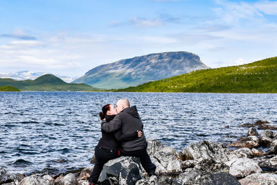 Rear view of men on rock by mountain against sky