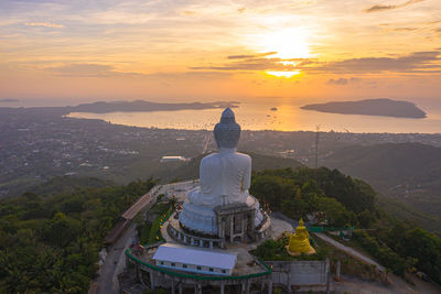 Buddha statue amidst buildings against sky during sunset