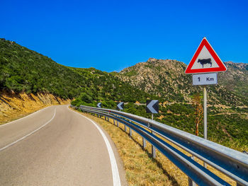 Road sign by trees against clear blue sky