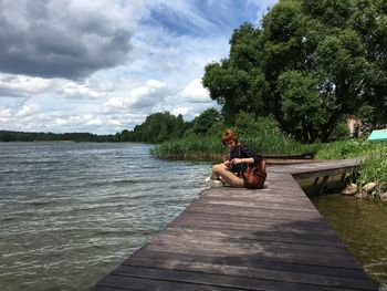 Full length of woman sitting on wooden pier over lake