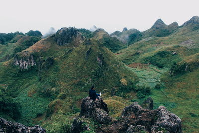 Man sitting on rock against sky