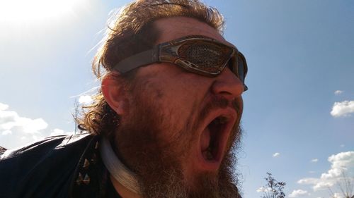 Close-up of bearded angry man screaming against sky